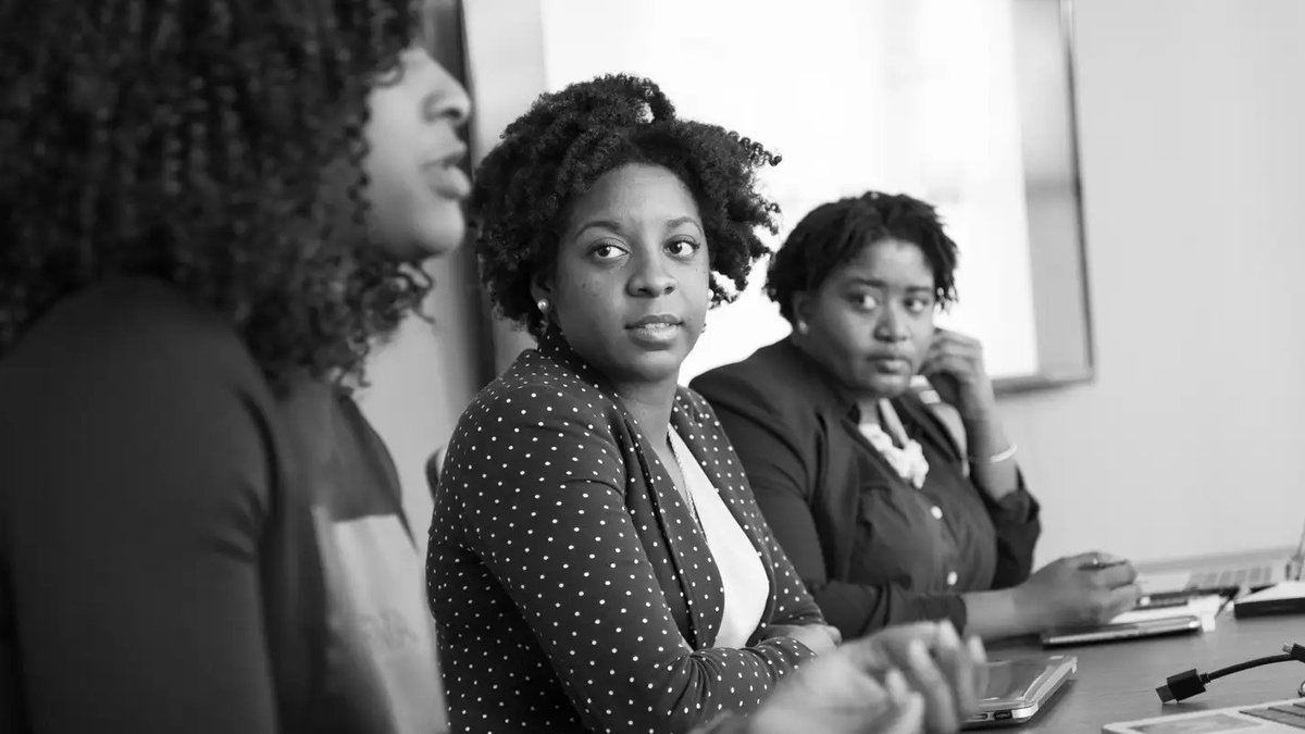 Jovem mulher negra em uma estação urbana olhando anúncios de emprego no celular.