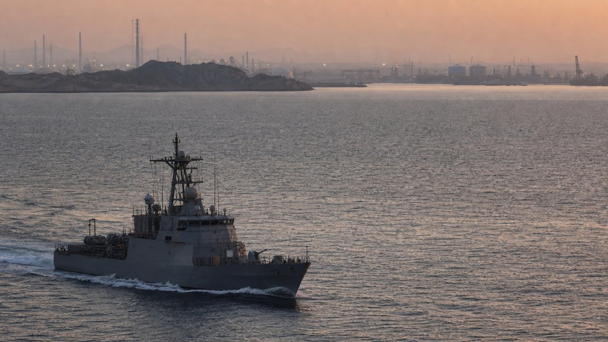 Navios militares patrulham aguas do Golfo ao amanhecer, com plataforma costeira ao fundo em clima de tensao.