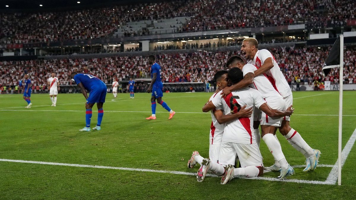 Jogadores do Peru comemoram gol enquanto atletas do Haiti lamentam em amistoso de futebol.