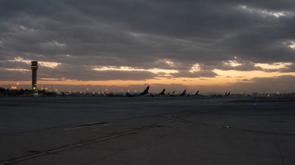 Aeroporto no Oriente Médio com pista vazia ao entardecer e céu carregado ao fundo.