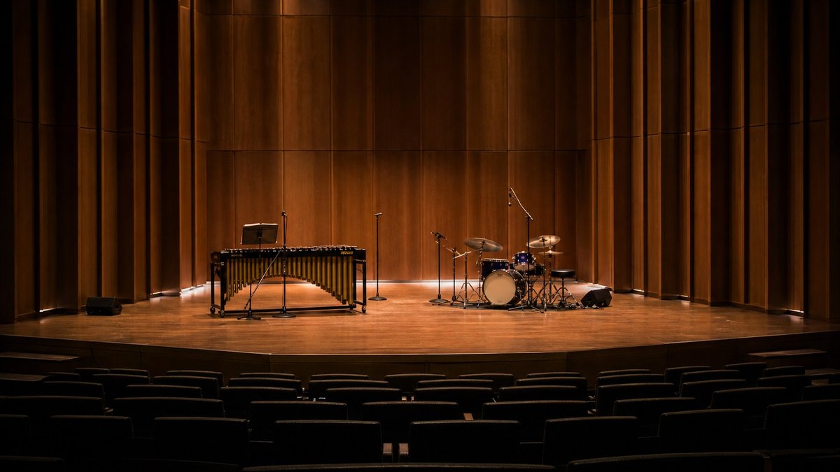 Palco vazio de teatro com vibrafone e bateria preparados para apresentação de jazz.