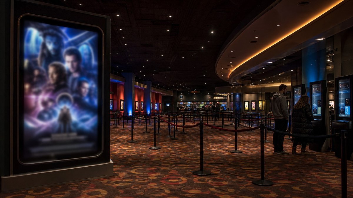 Lobby de cinema com cartazes desfocados e filas vazias em noite de estreia.