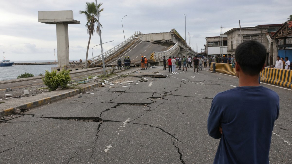 Rua costeira danificada por terremoto nas Filipinas com equipes de emergência avaliando rachaduras e destroços