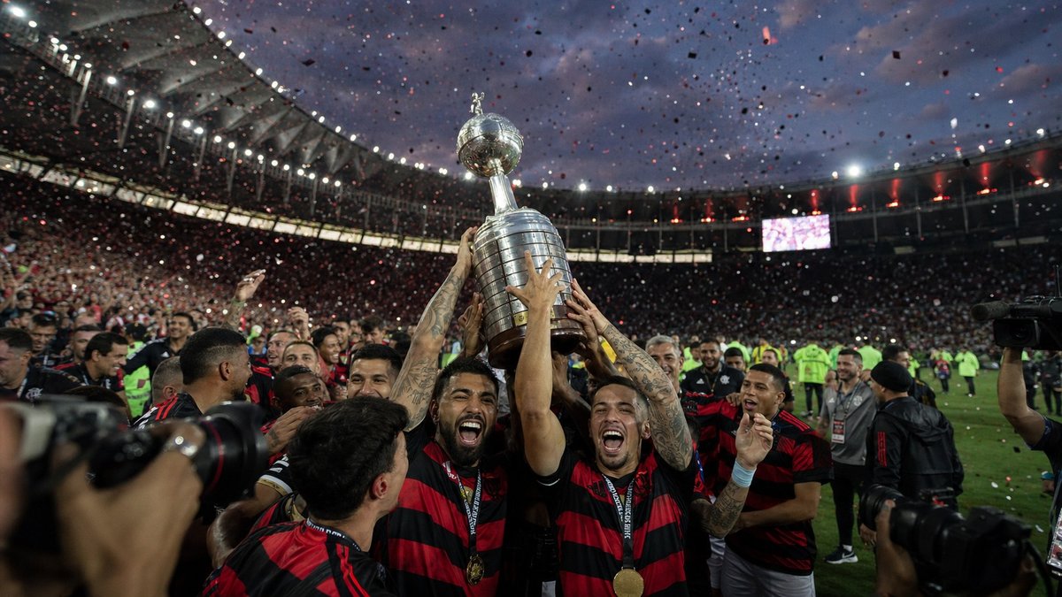 Jogadores de futebol em uniformes rubro-negros levantam troféu em estádio cheio